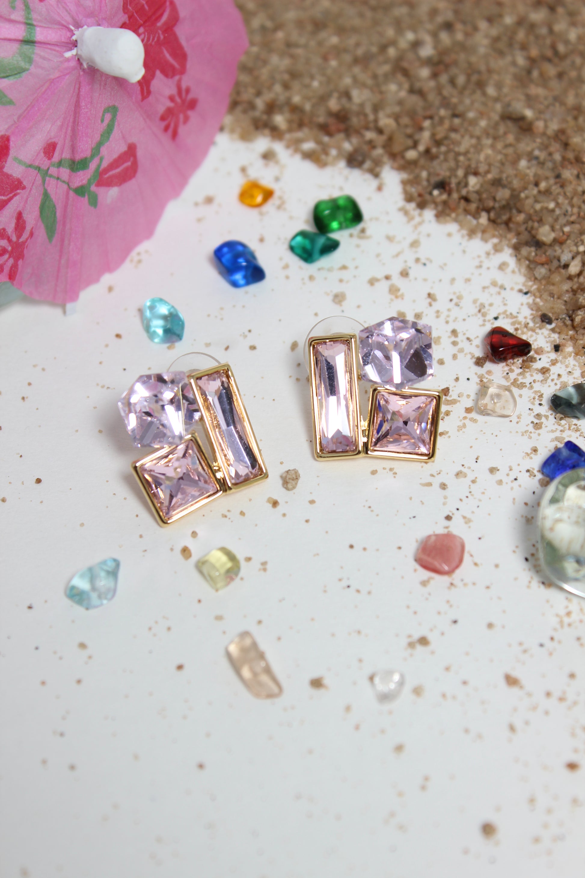 Blush Glow Earrings on a textured surface with small colorful stones and a pink parasol
