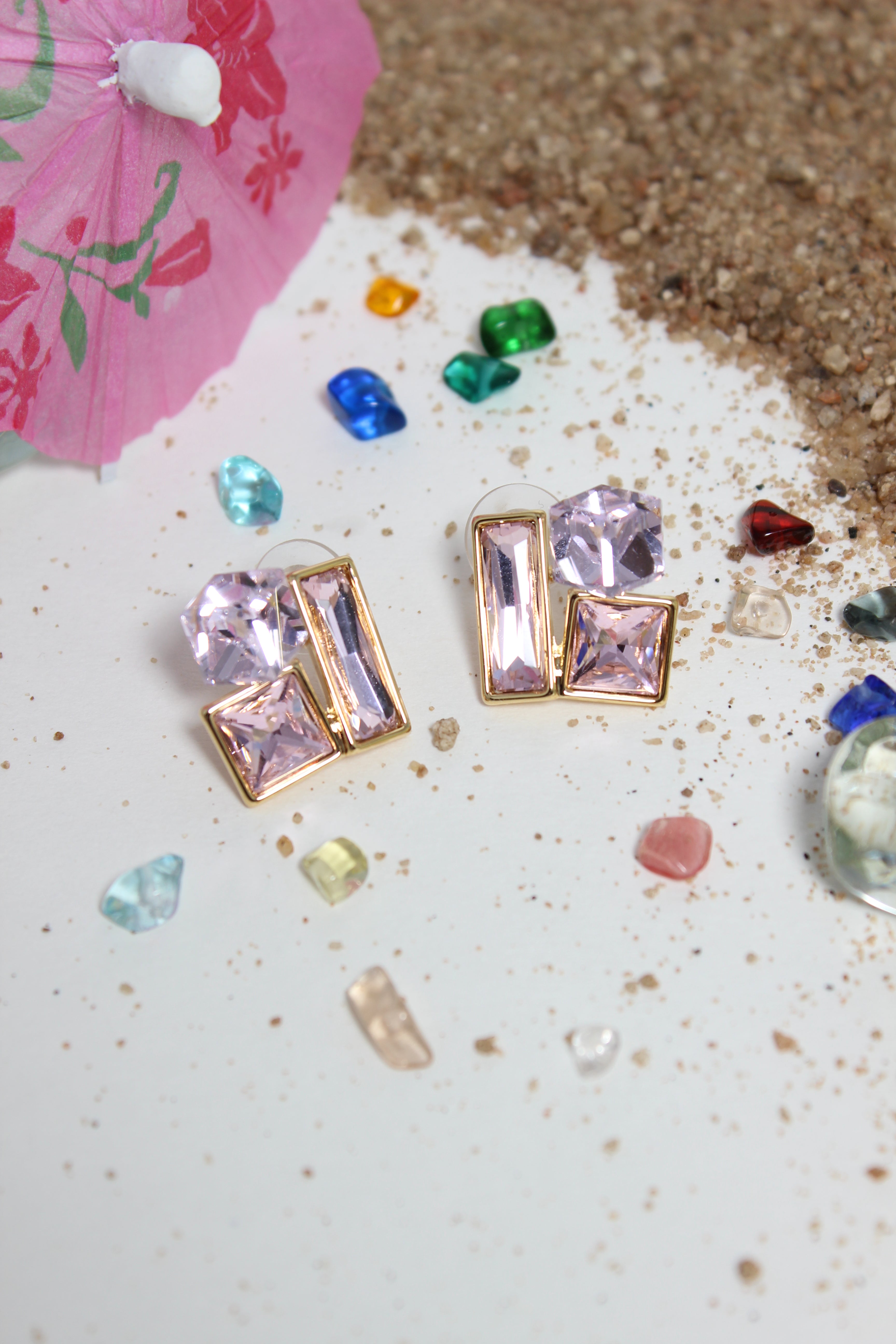 Blush Glow Earrings on a textured surface with small colorful stones and a pink parasol