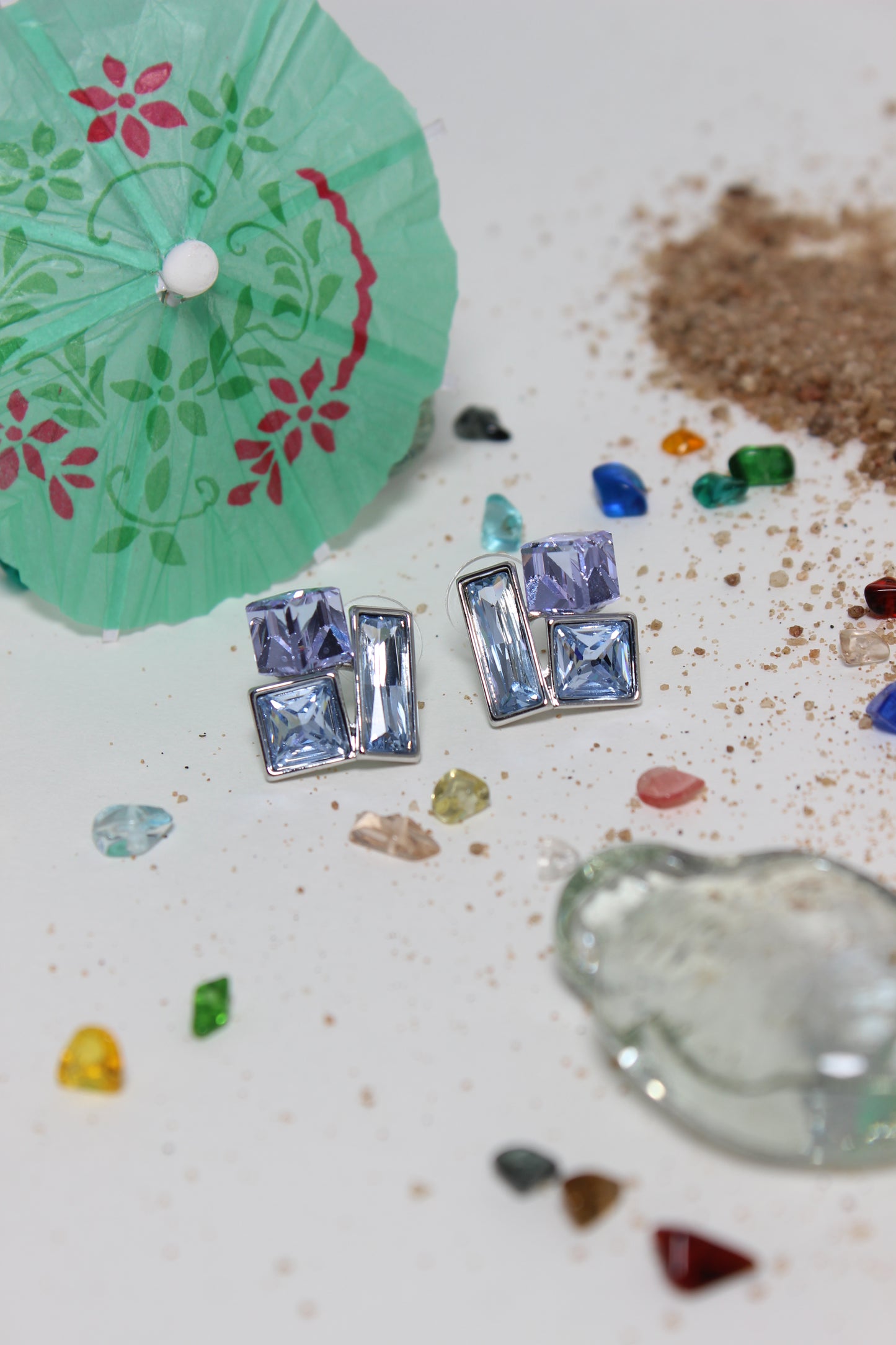 Twilight Glow Earrings on a textured surface with a green paper umbrella and colorful stones