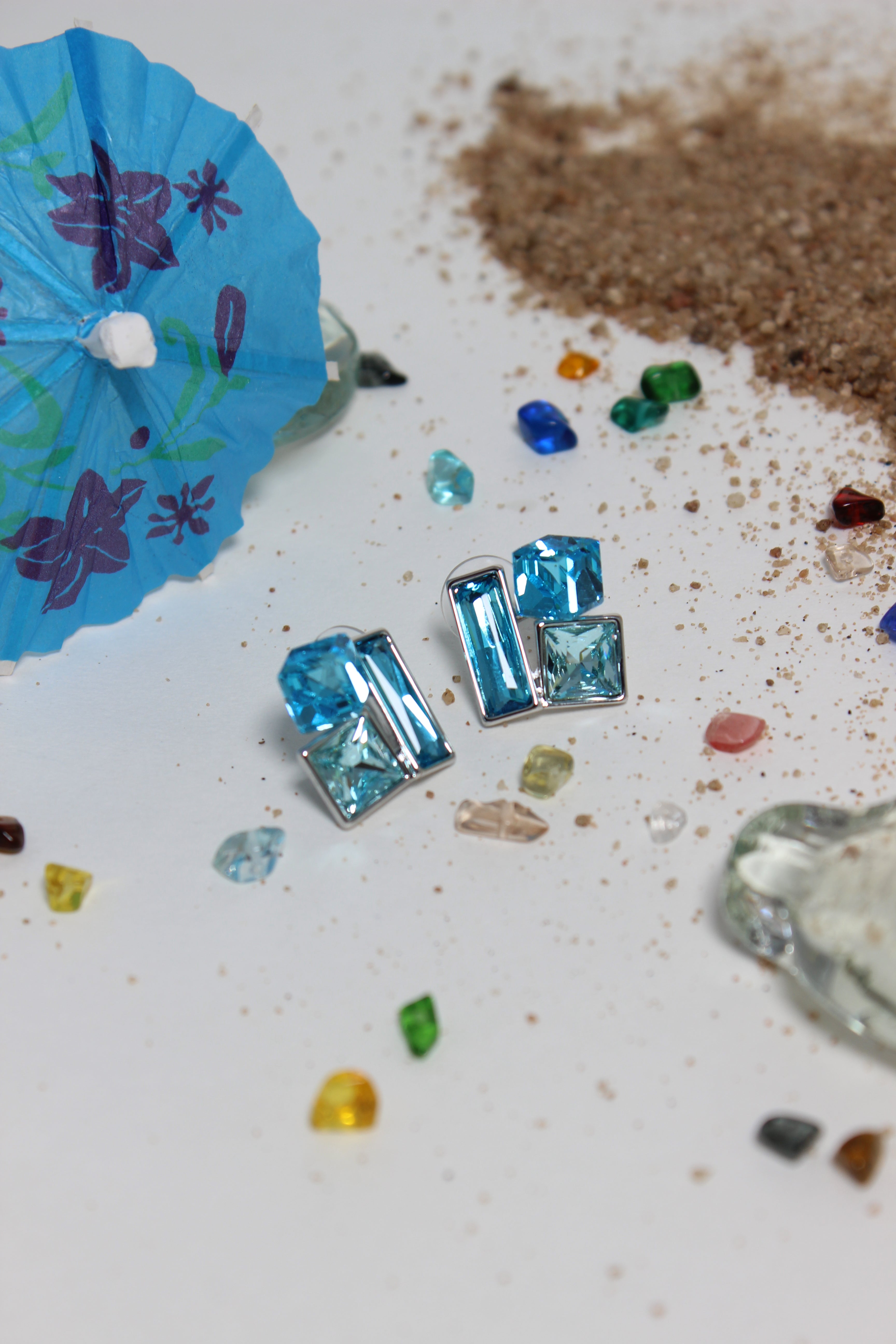 Azure Glow Earrings on a textured surface with sand and small stones