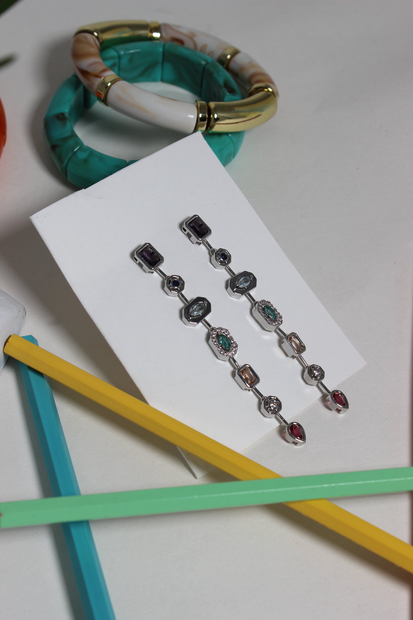 Argent Pastel Pour Earrings on a white card with colorful pencils in the background