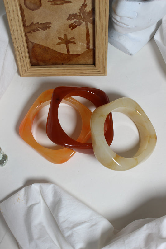 Fizz Resin Bangles on a white surface with a wooden frame and fabric in the background