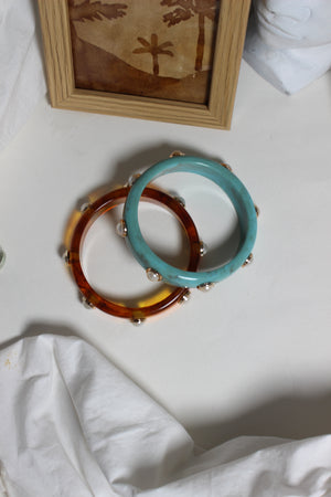 Confetti Stacks Resin Bangles on a light surface with a wooden frame and white fabric in the background