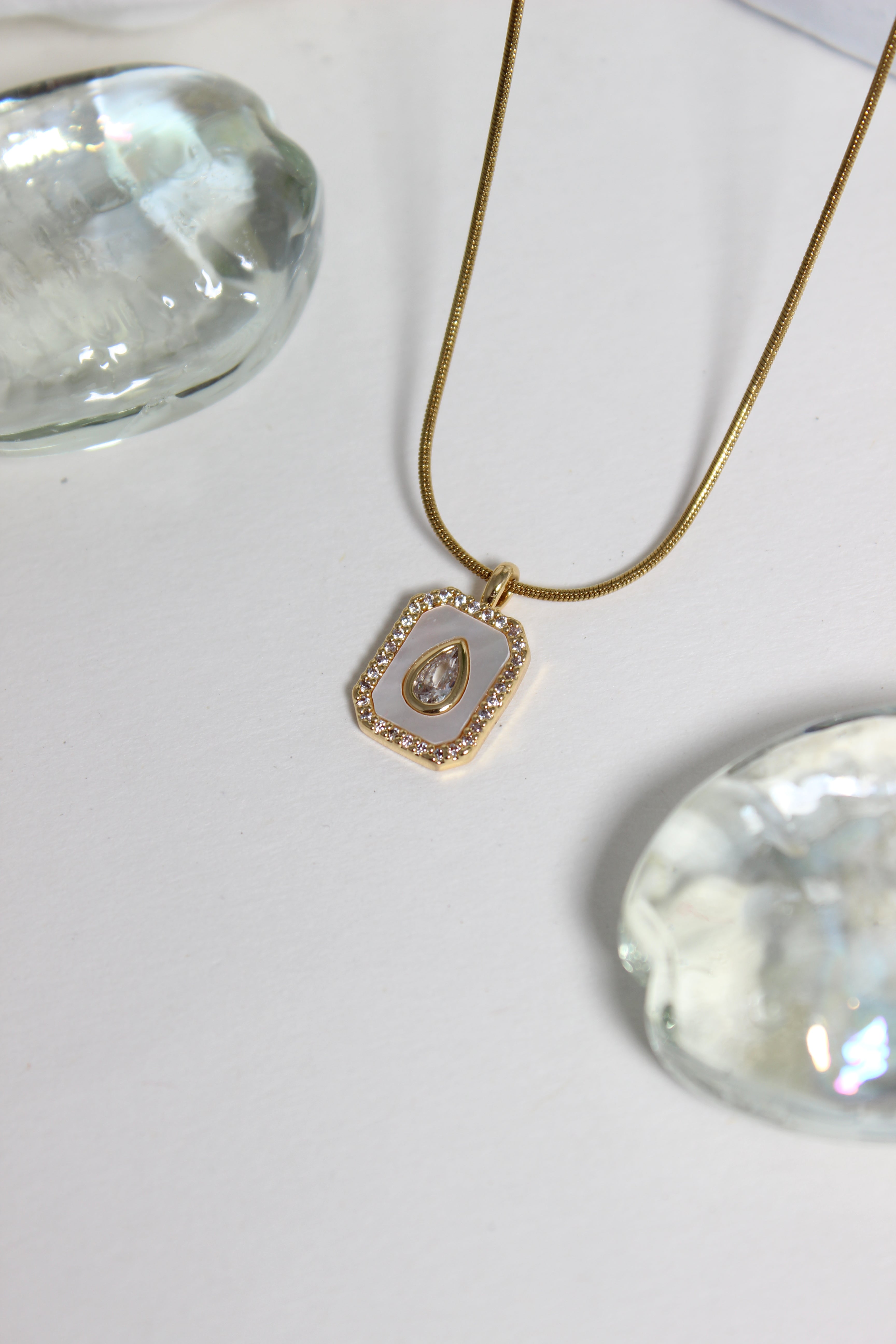 Oro Emeraude Glow Pendant Necklace on a white background with seashell 