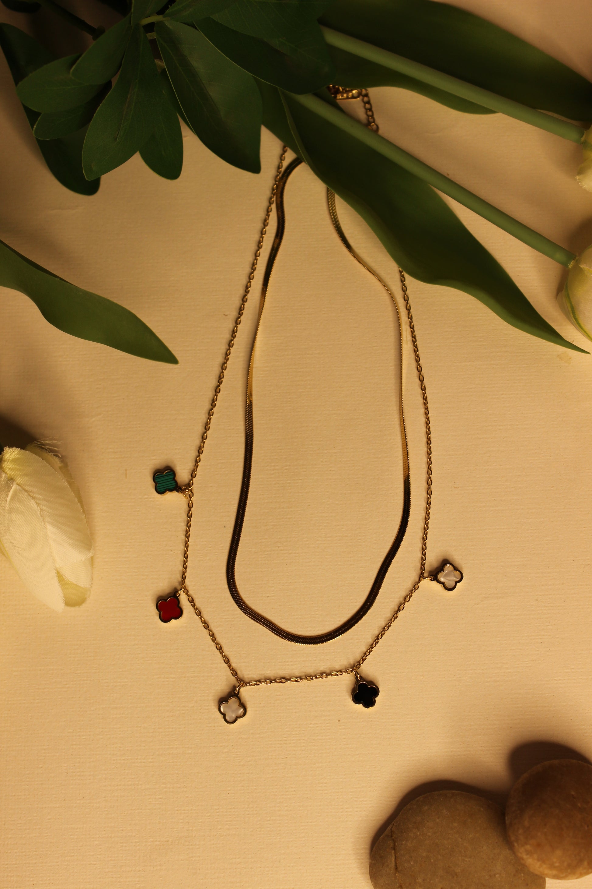 Charm Cascade Necklace on a beige surface with flowers and stones 