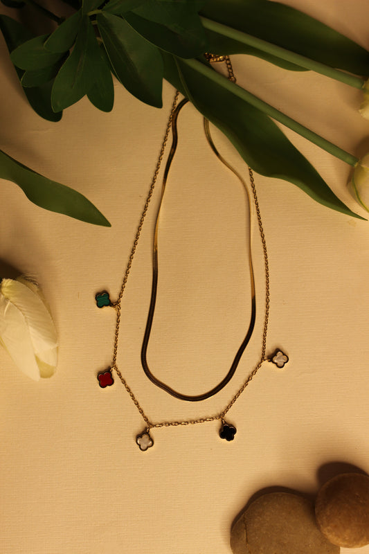 Charm Cascade Necklace on a beige surface with flowers and stones 