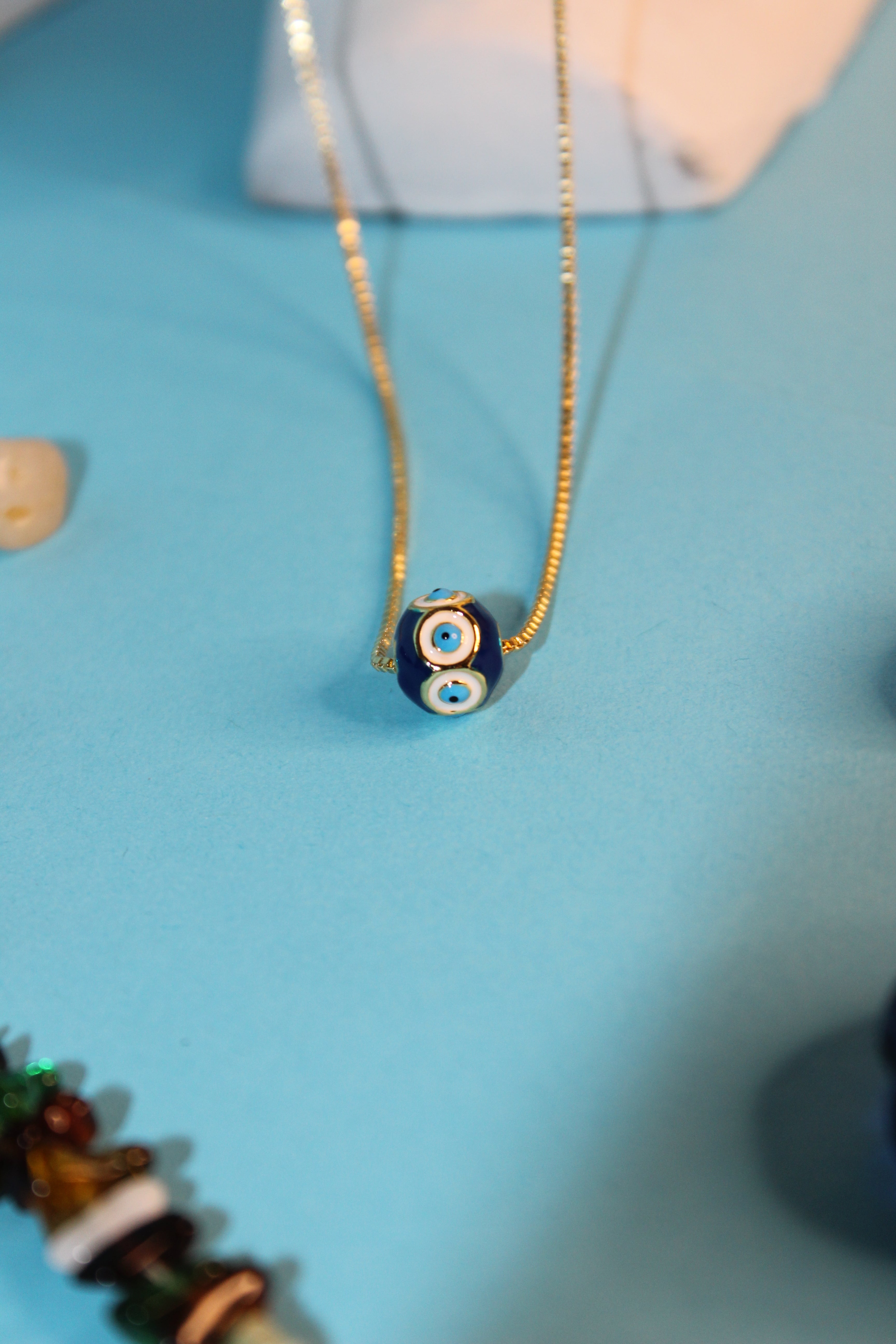 Close-up of a decorative glass bead on a Evil Eye Gem Pendant Necklace against a blue background