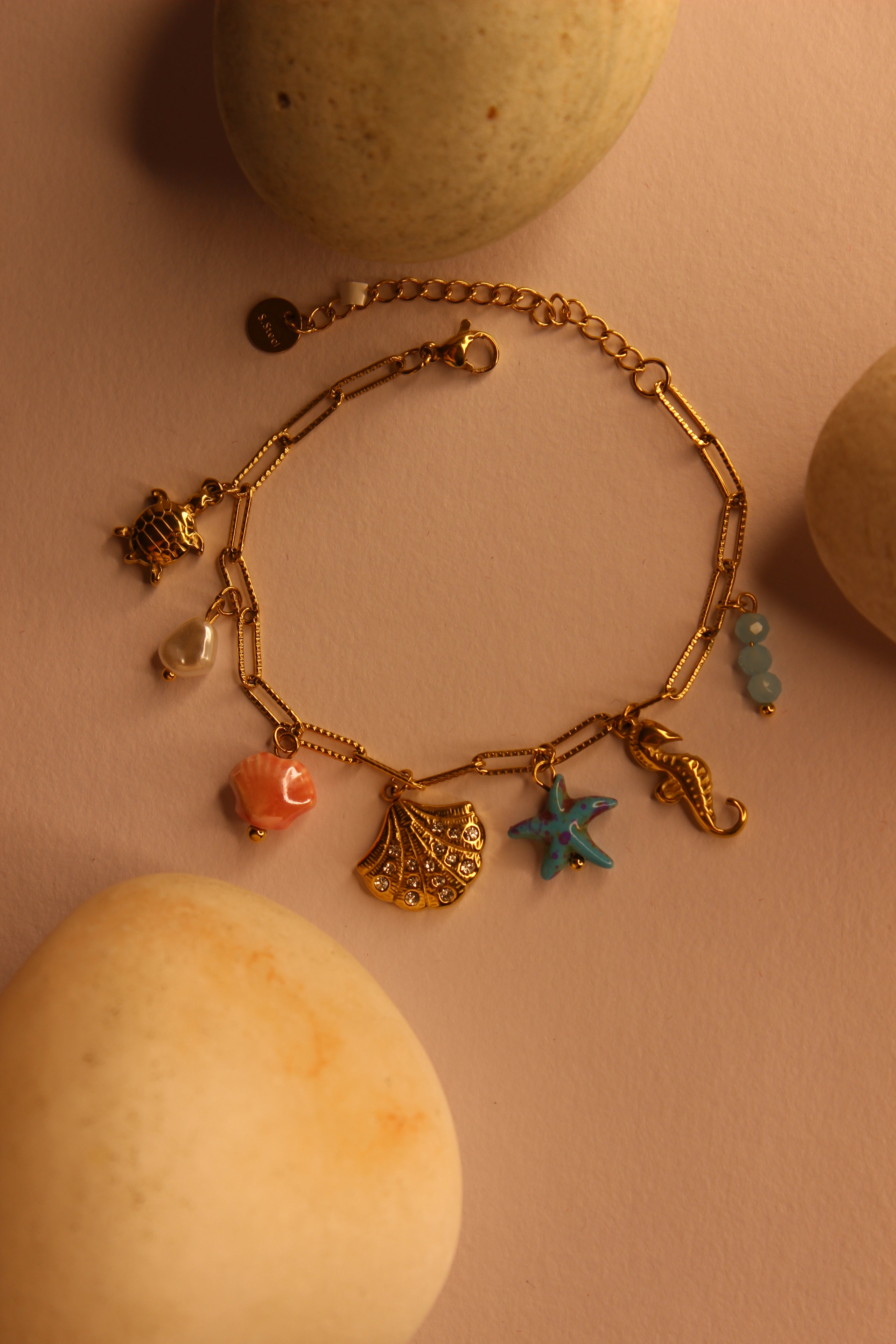 Oricca Charms Bracelet on a pink surface with stones