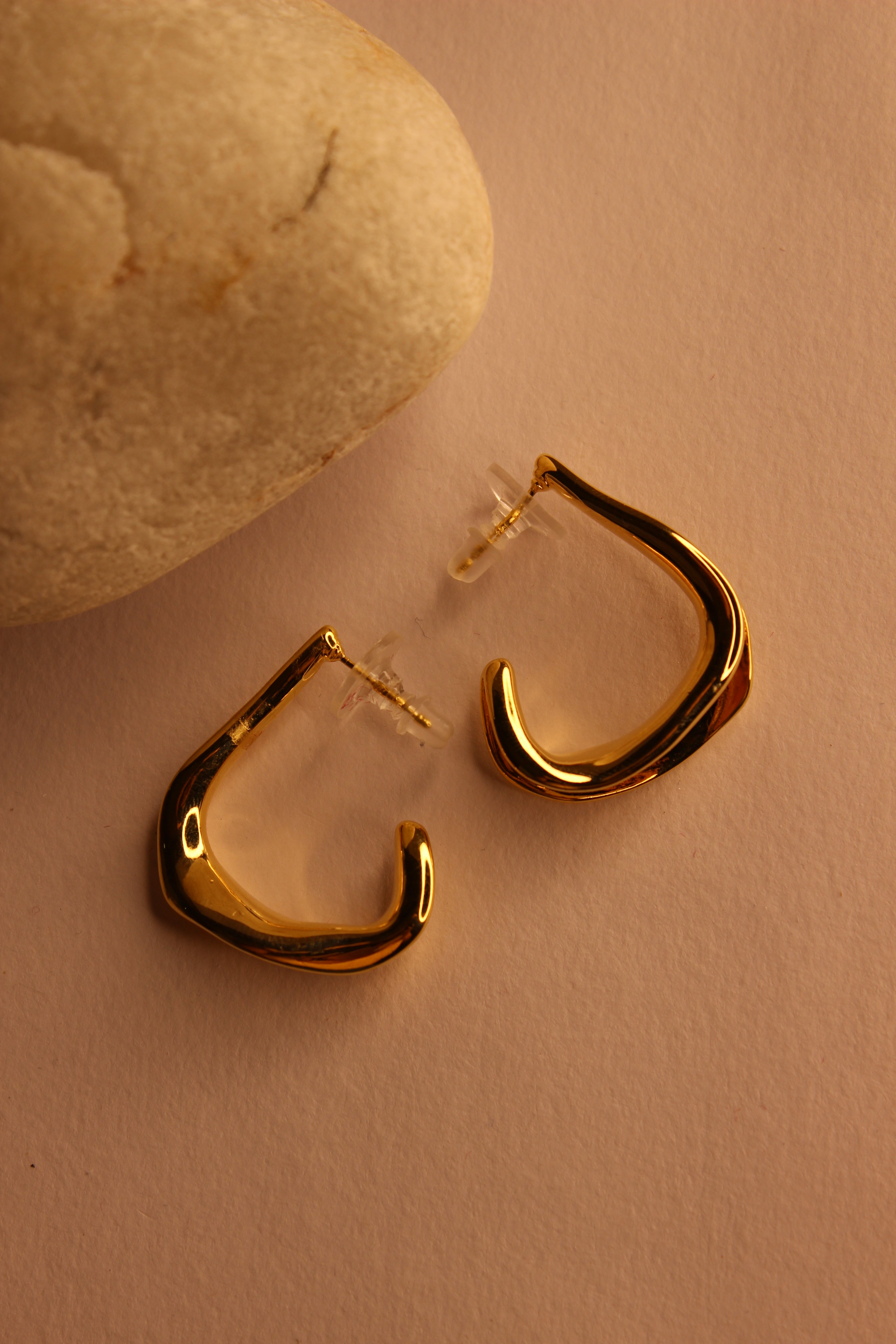 Spinelle Half Hoop Earrings on a textured beige surface