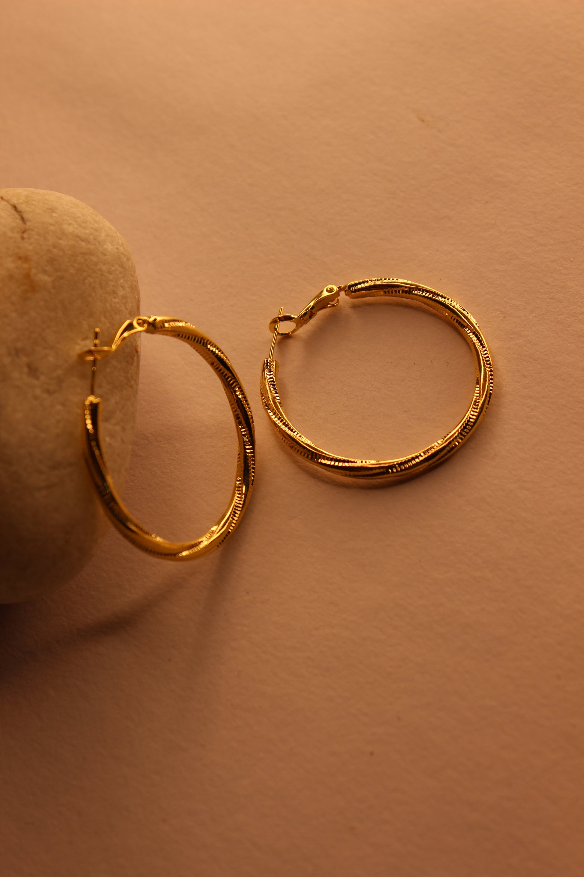 Two Twistline Hoop Earrings on a beige stone with a beige background