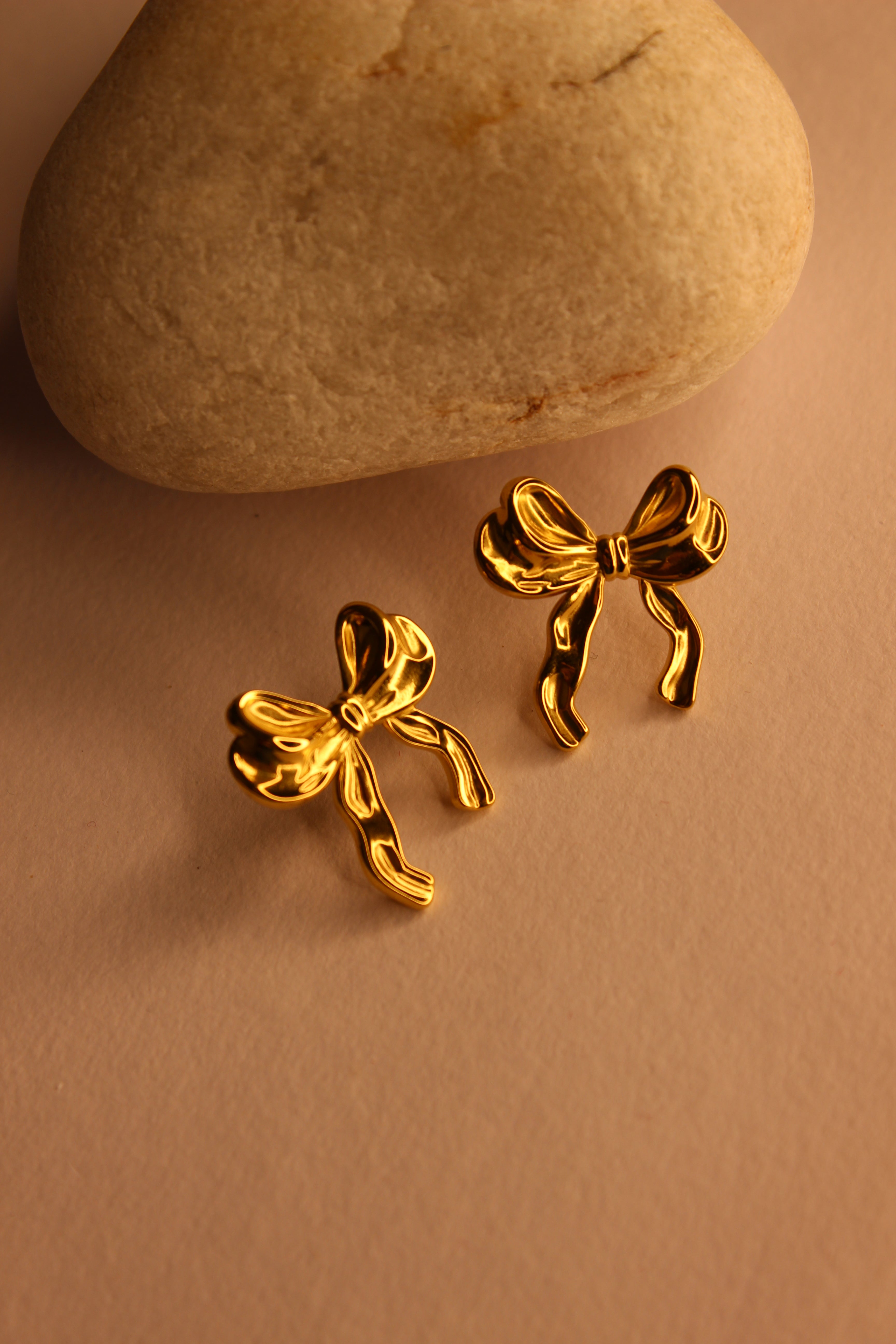 Goldtie Stud Earrings on a brown surface with a stone