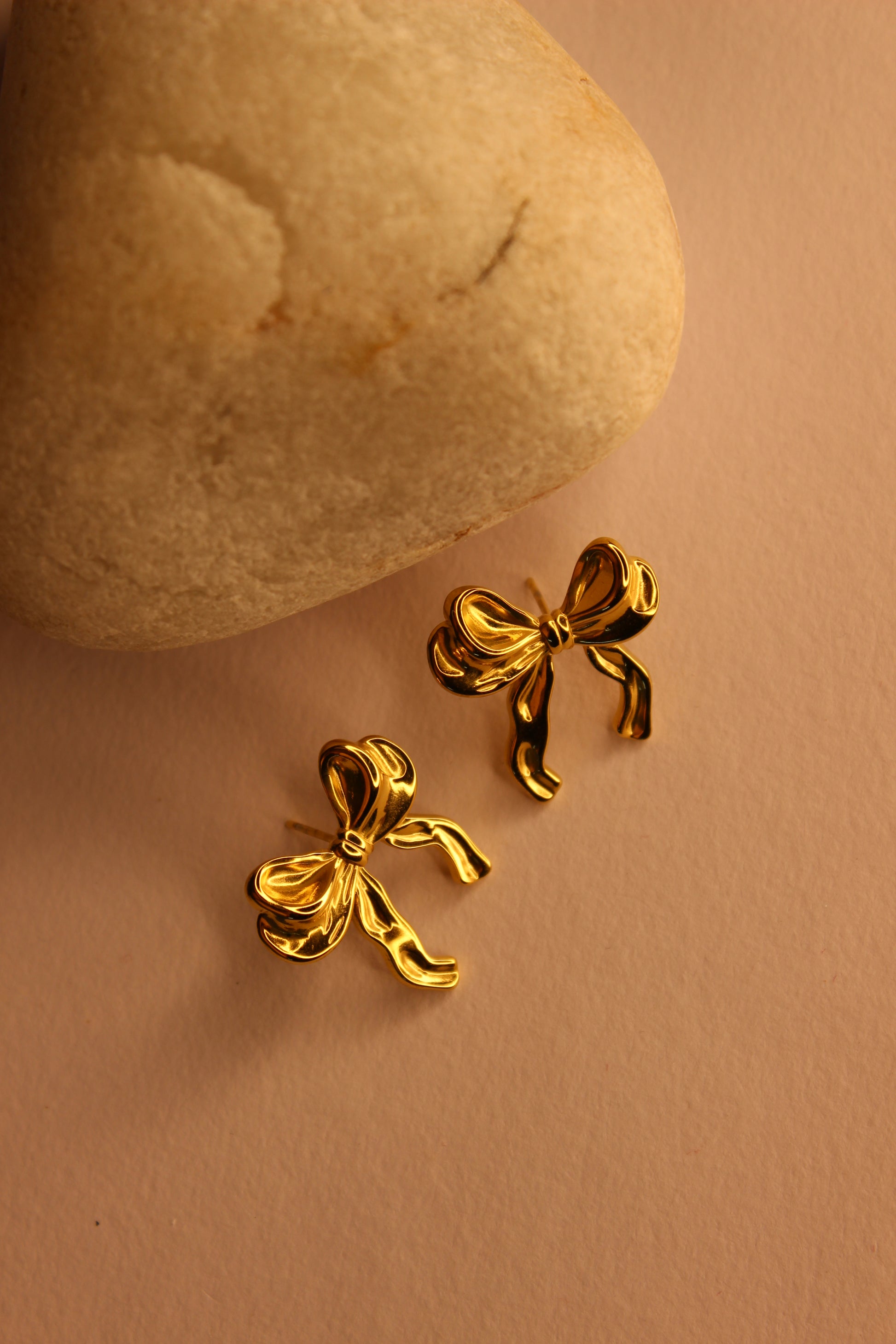 Goldtie Stud Earrings on a beige stone with a beige background