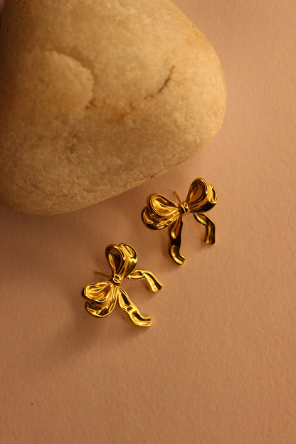 Goldtie Stud Earrings on a beige stone with a beige background