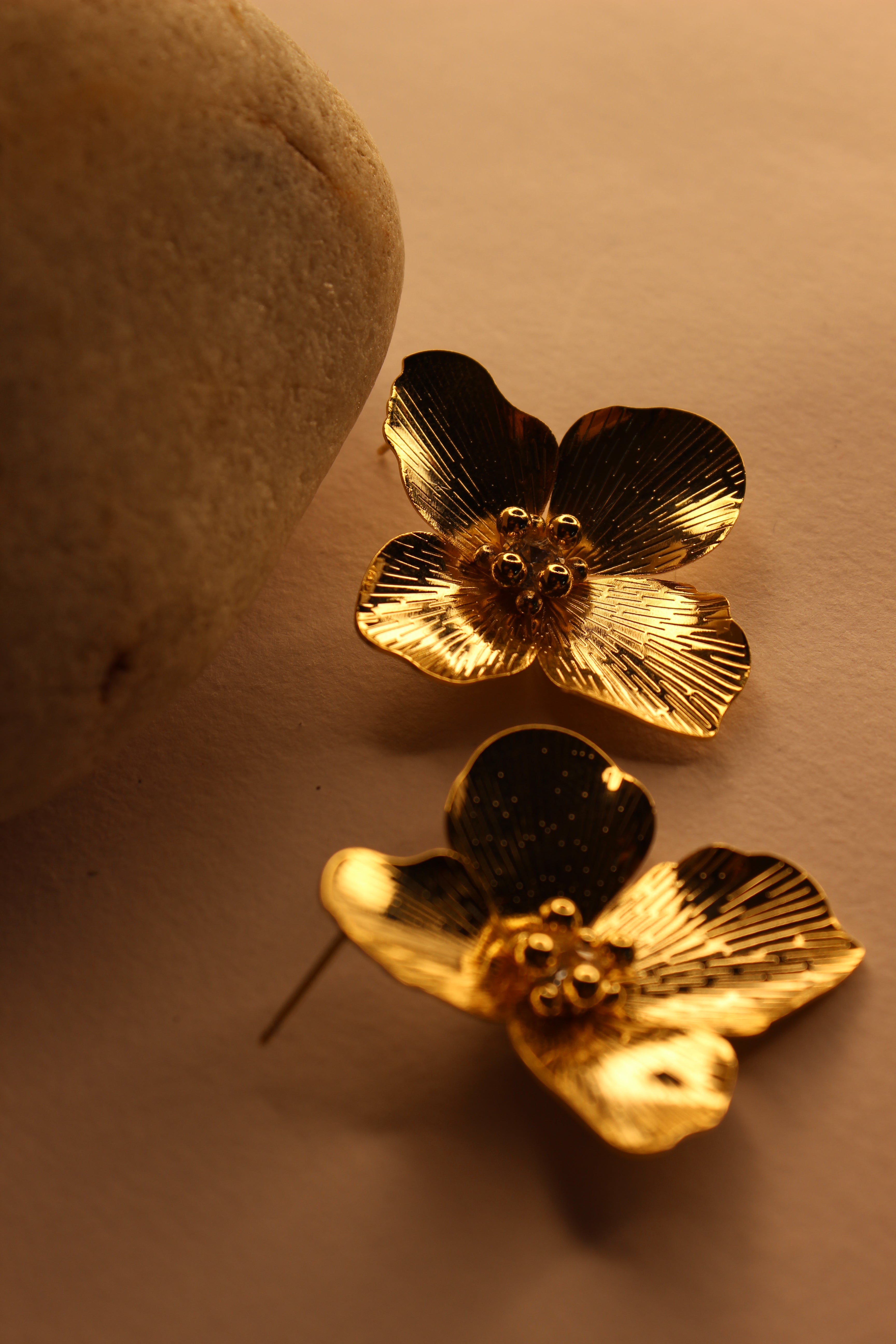 Pair of gold flower-shaped Pollene Earrings on a beige surface