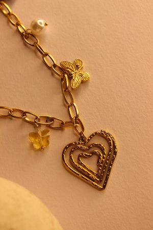 Hearts in Bloom Charms Necklace with heart, butterfly, and flower charms on a beige background