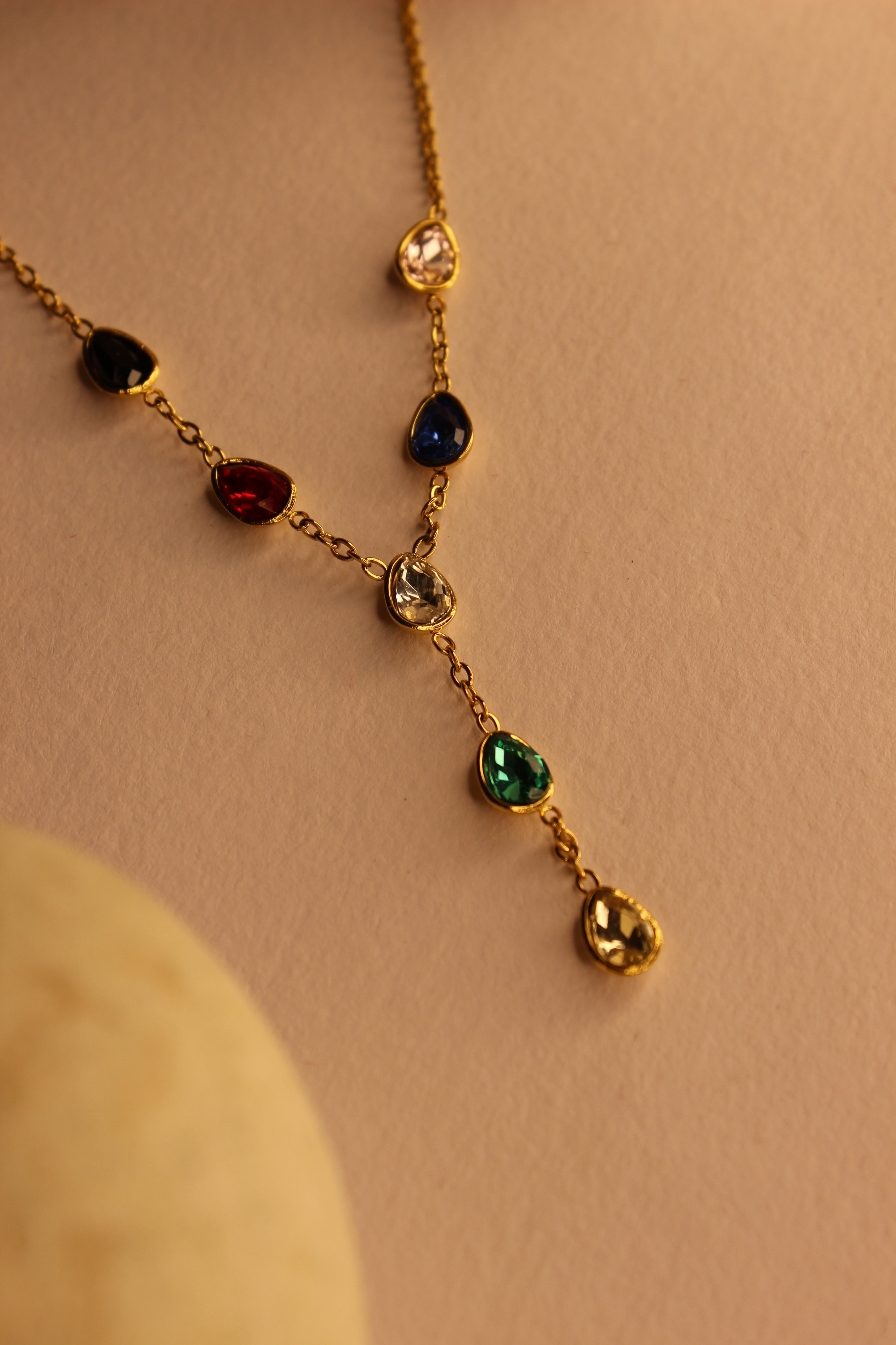 Prism Drop Necklace with colored gemstones on a beige background