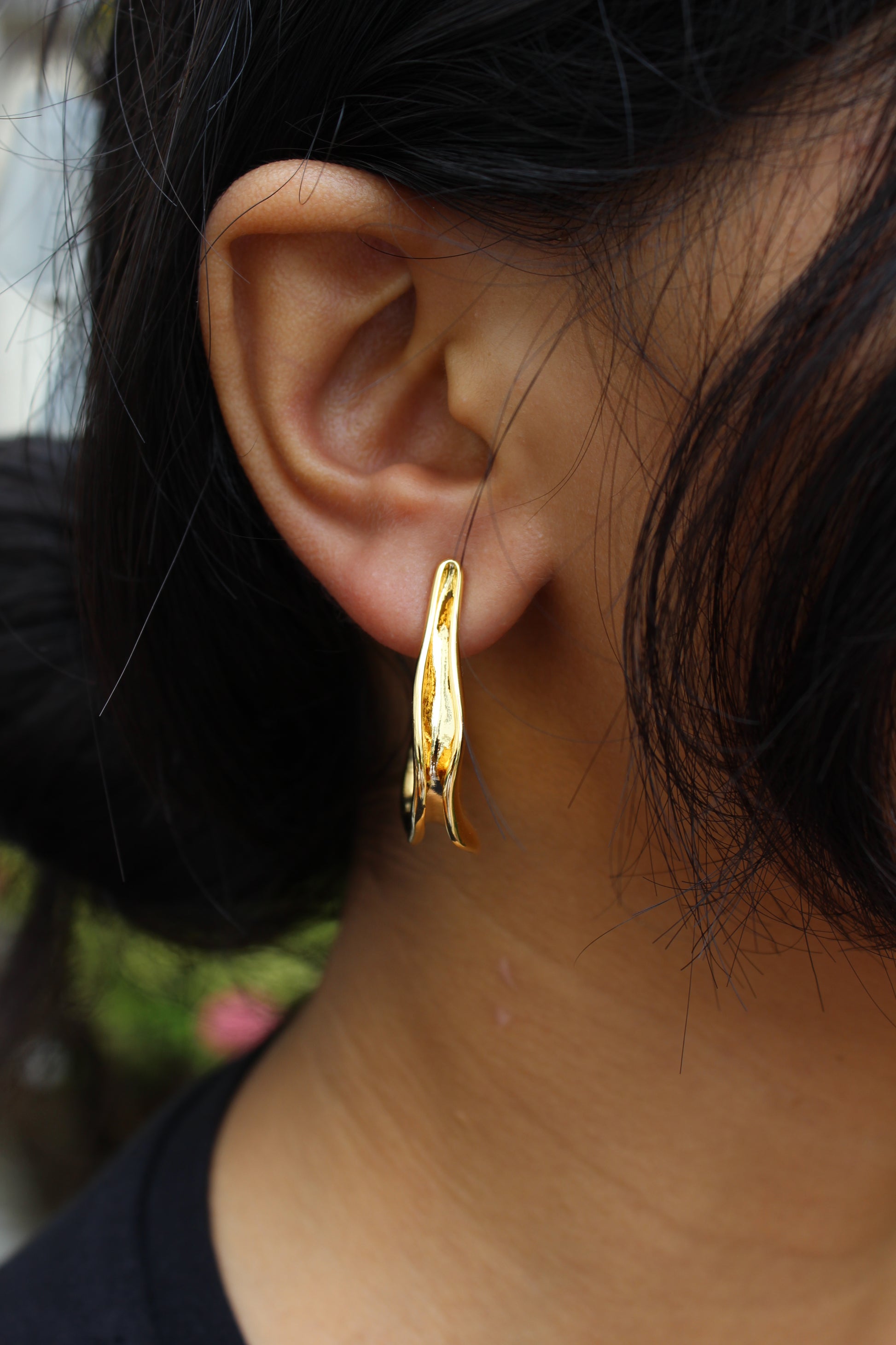 Close-up of an model wearing a Spinelle Half Hoop Earrings with a blurred background